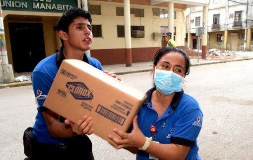 Ecuador earthquake - Red Cross passing bleach case in city- rubble